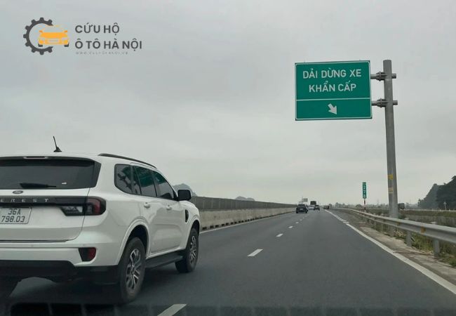 Một chiếc xe con dừng khẩn cấp trên cao tốc với đèn cảnh báo bật sáng, tài xế đang gọi điện. Một chiếc xe con dừng khẩn cấp trên cao tốc với đèn cảnh báo bật sáng, tài xế đang gọi điện.
